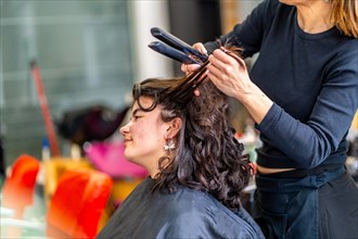 Profile of a caucasian beauty woman sitting in hair salon while hairstylist ironing the hair