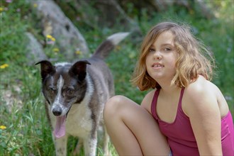 Beautiful eight year old girl in a red swimsuit with her dog looking at the floor smiling