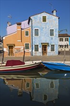 Moored boats on canal lined with orange, mauve and blue stucco houses, Burano Island, Venetian