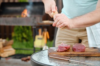 Unrecognizable man sprinkling salt from hand grinder on raw strip steak