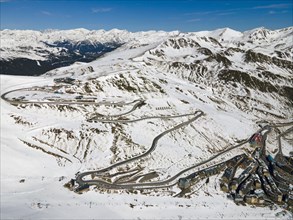 Snow-covered mountain landscape with serpentine road and settlement from a bird's eye view,