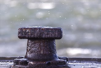 Rusty metal bollard in close-up with splashing water droplets and blurred background