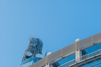 Large circular communication tower on roof of modern building with blue sky in background in South