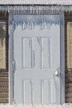 Storage shed door covered in thick ice and snow in residential backyard after ice storm in early
