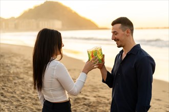 Side view of a romantic newlywed couple toasting during sunset on the beach