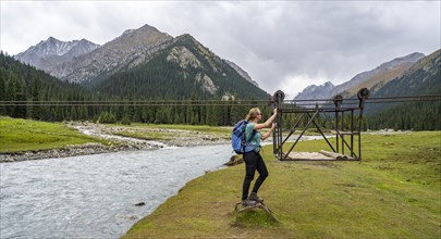 Hiker with backpack standing in front of a drawbridge in a mountainous landscape by the river,