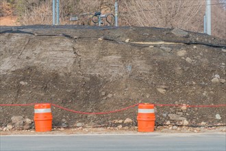 Orange traffic barrels in front of large pile of dirt covered with black mesh in South Korea