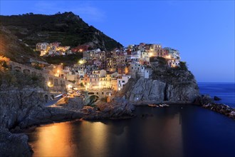 Nocturnal atmosphere over a quiet coastal town with shining windows and calm sea, Italy, Liguria,