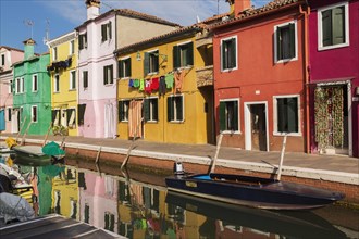 Moored boats on canal lined with pink, red, orange, yellow and green stucco houses decorated with