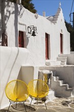 Two yellow modern designed chairs in front of building with small chapel, Mykonos Town, Mykonos