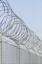 A grey security fence against a blue sky, topped with barbed wire