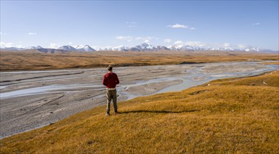 Young man in front of autumnal mountain landscape, meandering Sary Jaz river, high glaciated