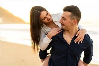 Horizontal close-up photo of a romantic couple piggybacking on the beach during sunset