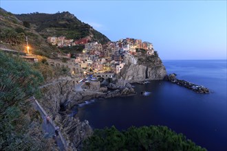 Mediterranean village on rocks on the coast at dusk with lights switched on and calm sea, Italy,