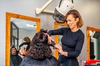 Hairstylist ironing the hair of a client in a salon next to a mirror with image reflected on it