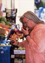 Older woman with gray hair and glasses in a market smelling a tomato