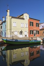 Moored green and blue boat on canal lined with yellow and red stucco houses, Burano Island,
