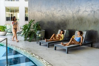 Two female friends are lounging in a fancy hotel pool area, laughing and enjoying themselves while