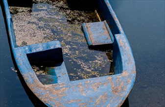 Closeup of blue fishing boat filled with dirty water floating in river
