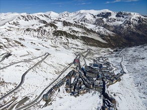 Aerial view of a ski resort with buildings and streets framed by snow-covered mountains, El Pas de