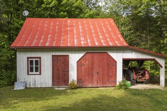 Old white vertical wood plank and red trim barn facade with red standing seam sheet metal roof,