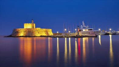 Historic castle with lighthouse at night, reflecting in the water next to a yacht, night shot, Fort