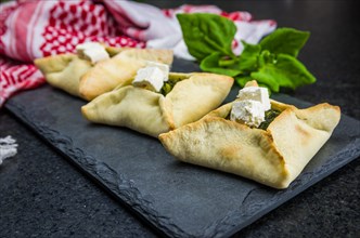 Delicious Lebanese (Arabic) food, spinach sfiha with ricotta cheese on a black slate stone