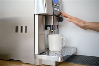 Female hand presses coffee button in coffee machine