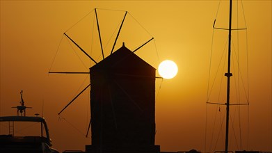 Silhouette of a windmill in front of the rising sun with a warm colour gradient, twilight, Mandraki