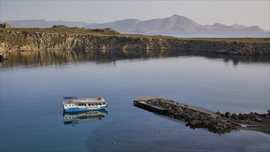 View of a quiet harbour with a boat and surrounding cliffs in the evening light, Lindos, Rhodes,