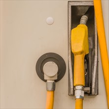 Closeup of gas pump handle with yellow rubberized cover inserted into side of gas pump in South
