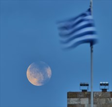 Full moon in semi-darkness next to a blurred flag at dusk, twilight, Mandraki harbour, Rhodes,