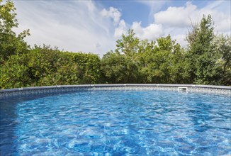 Above ground swimming pool surrounded by deciduous trees in residential backyard, Quebec, Canada,