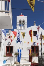 Greek Orthodox church and colourful flags hanging over narrow alley in Mykonos Town, Mykonos