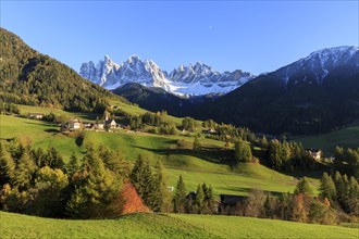A small settlement nestled in an autumnal meadow landscape with a panoramic view of the Dolomites,