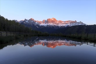 The sunset bathes the mountain peaks in warm light that is reflected in the lake, Trentino-Alto