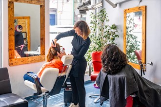 Full length photo of a smiling female hairdresser talking with woman while combing a client in a