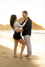 Vertical photo of a young caucasian couple looking at each other standing on the beach during
