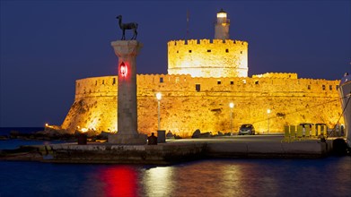 Illuminated historic fortress by the sea at dusk with clear sky and lighthouse, night shot,