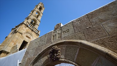 Stone arch in front of a historic church tower under a bright blue sky, Panagia Church, St Mary's