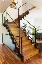 Black powder coated steel L-shaped staircase with stained and varnished wooden steps and tempered