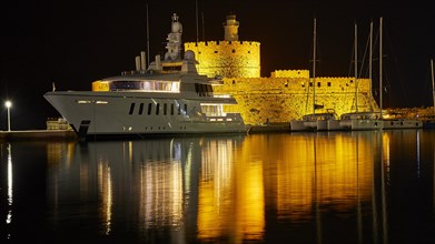 Night scene of an illuminated castle and a lighthouse with reflections near a yacht, night shot,