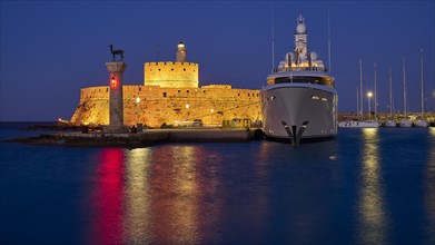 An illuminated castle and a luxury yacht lie by the sea at night with glowing reflections in the
