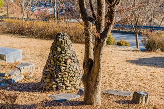 Pile of stones in the shape of an upside down cone next to a tree in a public road side park near