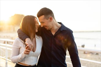 Tender young caucasian couple embracing strolling along a promenade during sunset