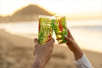Close-up of hands of lovers toasting with glasses during sunset on the beach