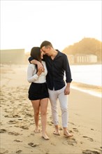 Vertical photo of a young caucasian tender couple embracing on the beach during sunset