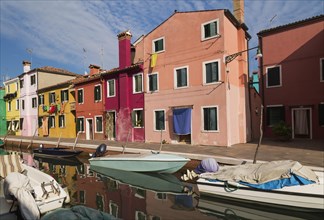 Moored boats on canal lined with pink, red, orange, yellow and green stucco houses decorated with