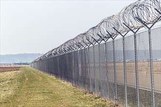A long security fence with barbed wire in a field under a clear sky