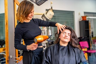 Professional smiling hairdresser drying the long hair of a relaxed woman in the hair salon